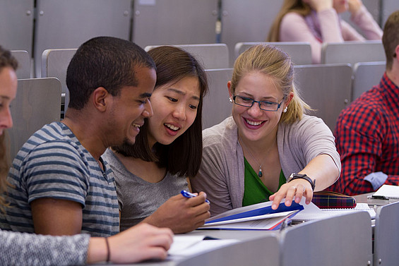 Internationale Studierende sprechen miteinander sitzend in einem Hörsaal.