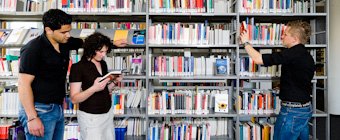 Symbolfoto: Menschen vor Bücherregalen einer Hochschulbibliothek.