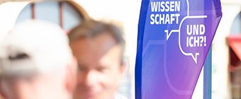 Zwei Männer stehen sich gegenüber und unterhalten sich. Im Hintergrund ist eine Beach Flag mit der Aufschrift "Wissenschaft - und ich?!" zu sehen. Bildnachweis: BBAW