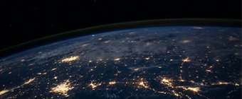 Foto einer Ansicht der Erde aus dem Weltraum während der Nacht. Zahlreiche Lichter von Städten und Ballungszentren sind klar erkennbar. Am Horizont zeichnet sich die dünne Atmosphäre ab, während darüber der schwarze Weltraum mit vereinzelten Sternen sichtbar ist.